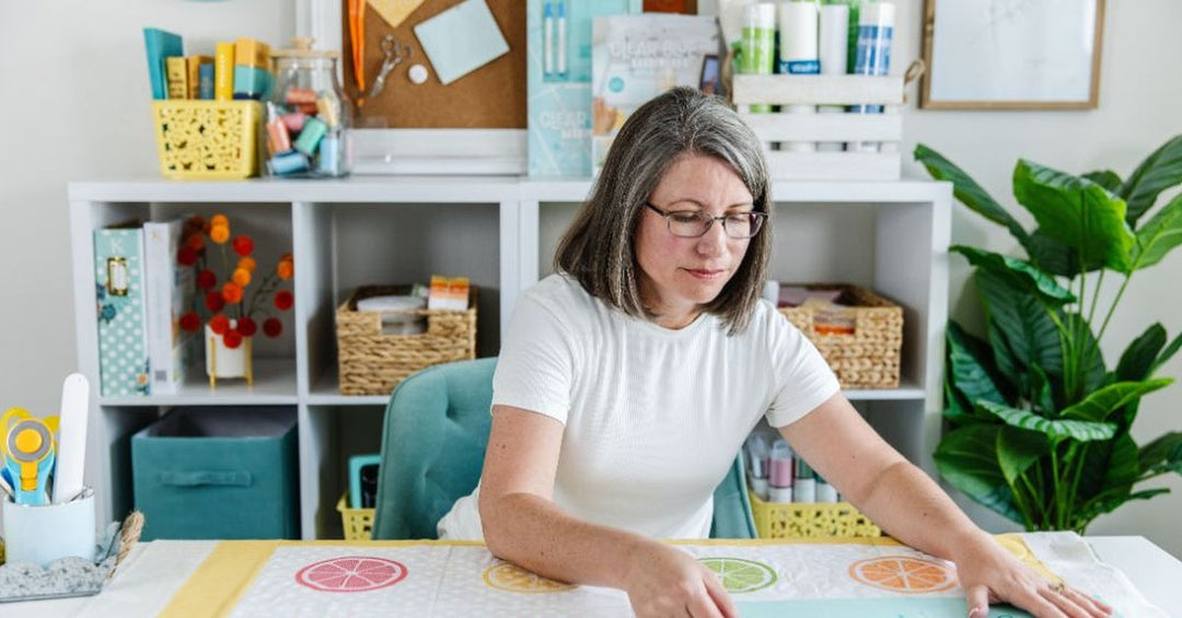 Person using a quilting template to mark and align colorful citrus-themed quilt blocks, helping ensure accurate placement and consistent quilt patterns.