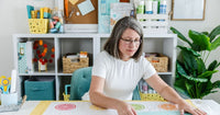 Person using a quilting template to mark and align colorful citrus-themed quilt blocks, helping ensure accurate placement and consistent quilt patterns.