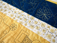 Blue, white, and gold embroidered fabric strips with outlined sports shapes, pom poms, and large "GO TEAM" lettering.
