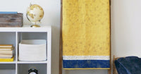 Yellow quilt draped over a wooden blanket ladder beside a white shelf with books, globe, clock, and basketball on the floor.