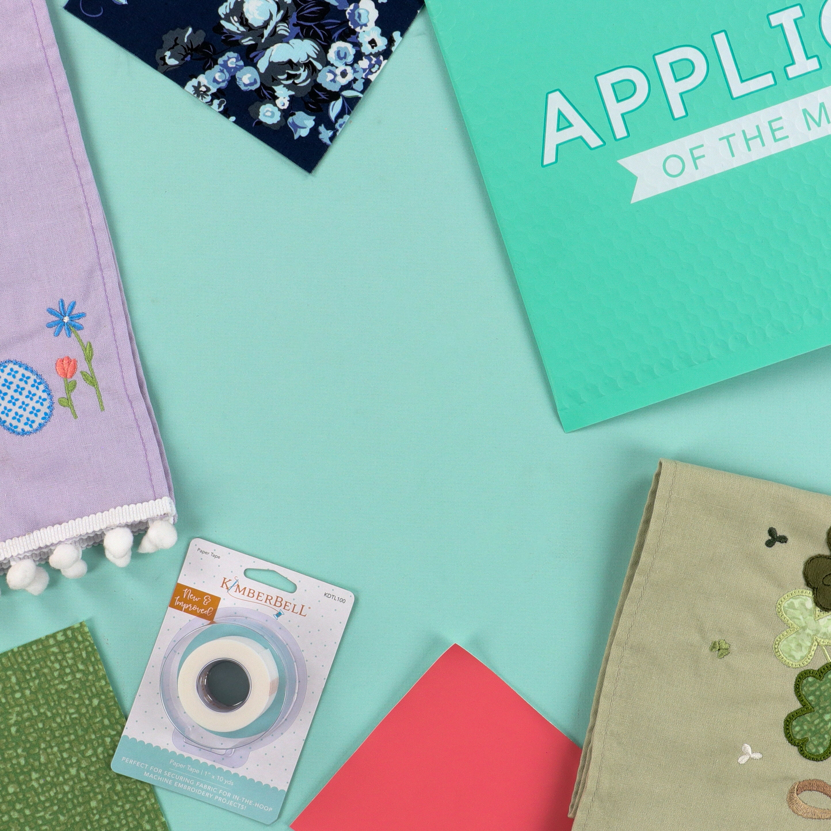 Collection of craft materials including fabric, a roll of tape, and a card on a teal background