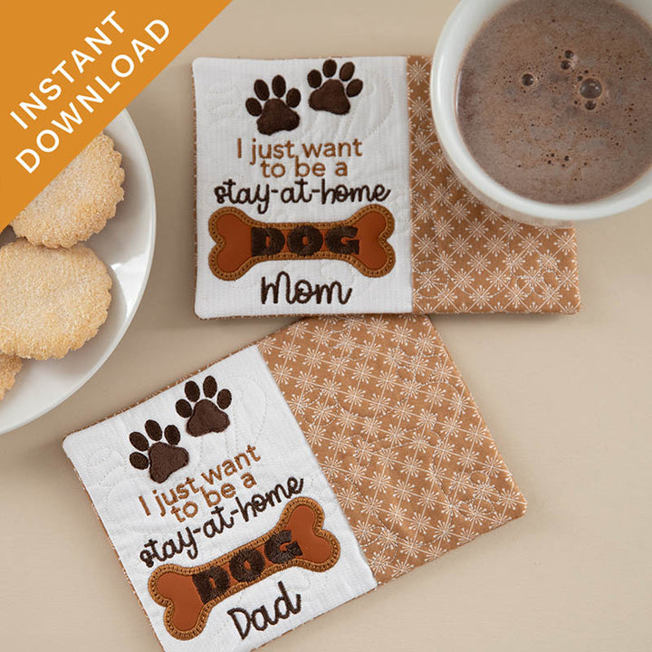 Two mug rugs with paw prints and text on a beige surface with a cup of hot chocolate and cookies.