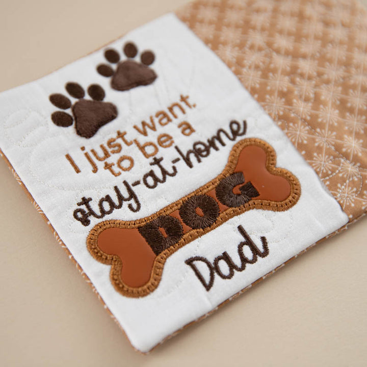 Embroidered mug rug with text 'I just want to be a stay-at-home dog dad' on a white background.