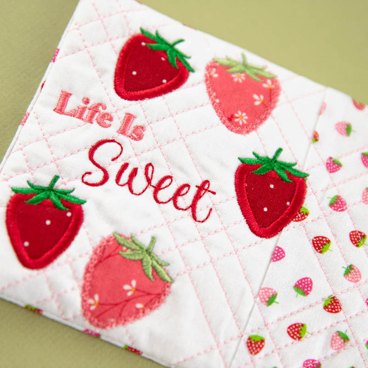Quilted mug rug with strawberry pattern and 'Life is Sweet' text on a green background