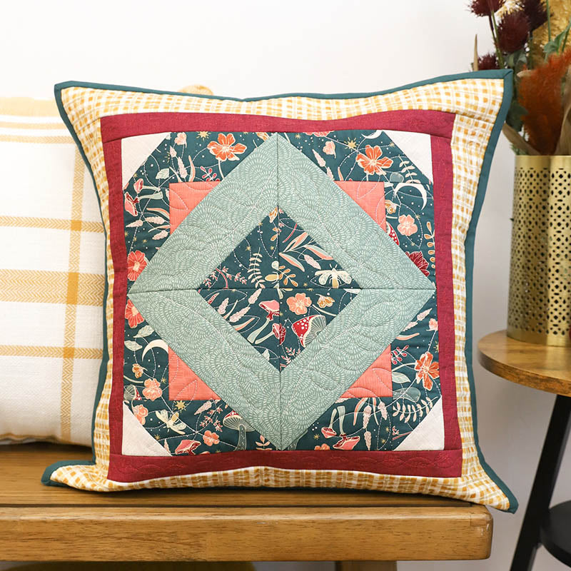 October 2025 Perfectly Pieced design on a pillow being displayed on a wooden bench.