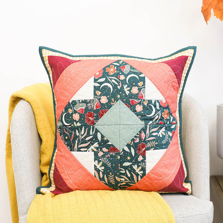 October 2025 Perfectly Pieced design on a pillow being displayed on a chair draped with a yellow blanket.