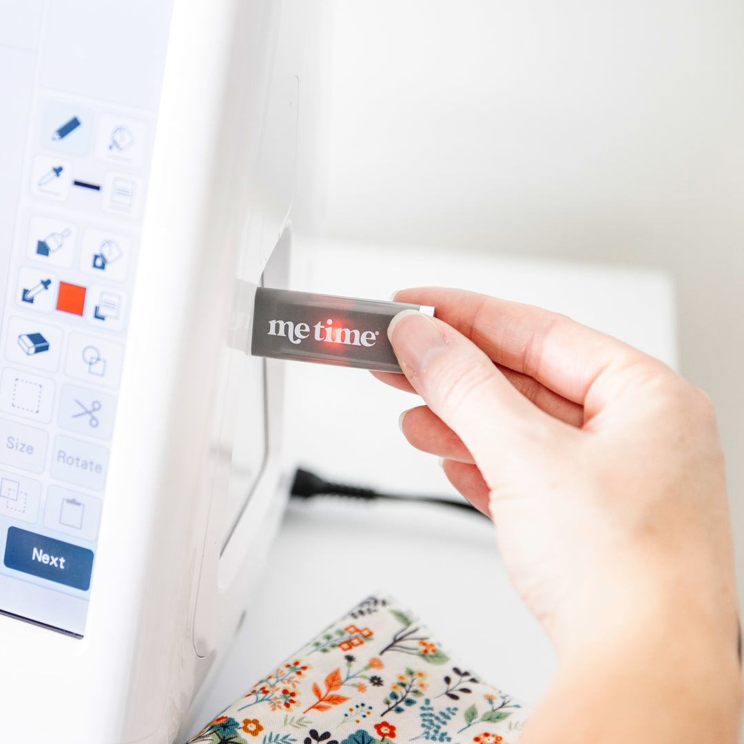Hand plugging in a 'Me Time' USB into an embroidery machine.