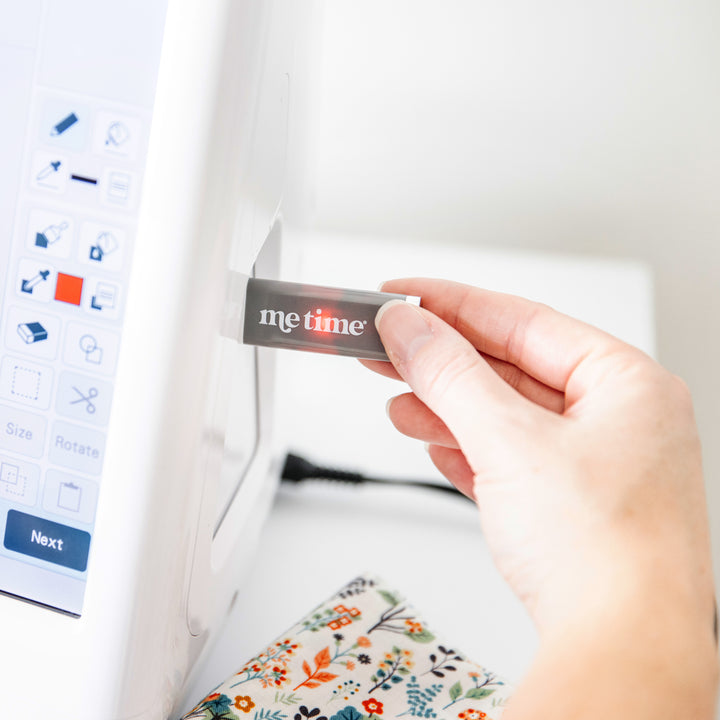 Hand plugging in a 'Me Time' USB into an embroidery machine.