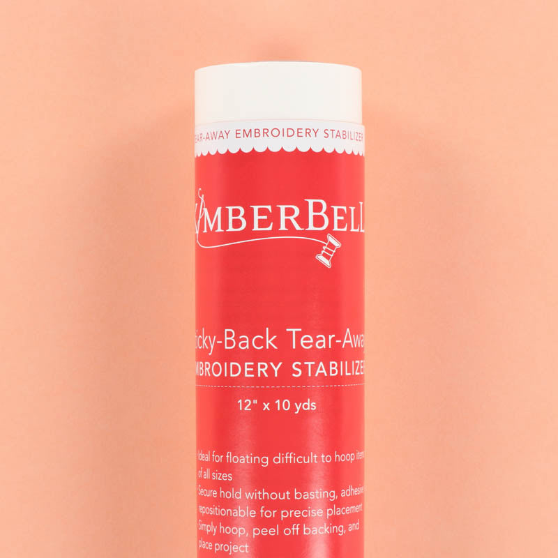 Red roll of Kimberbell embroidery sticky-back tear-away stabilizer on a peach background