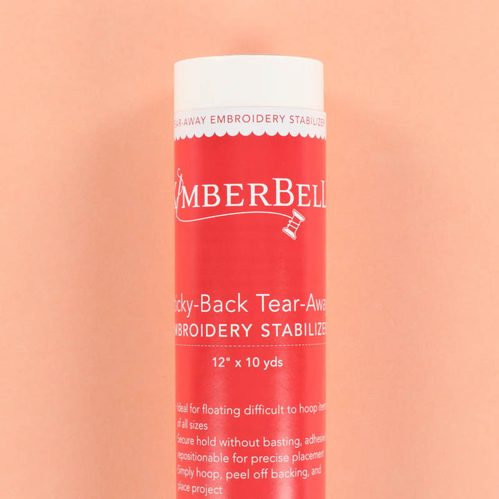 Red roll of Kimberbell embroidery sticky-back tear-away stabilizer on a peach background