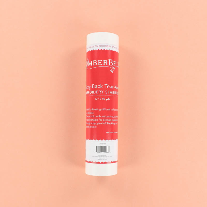 Red and white roll of Kimberbell Sticky-Back Tear-Away embroidery stabilizer on a peach background