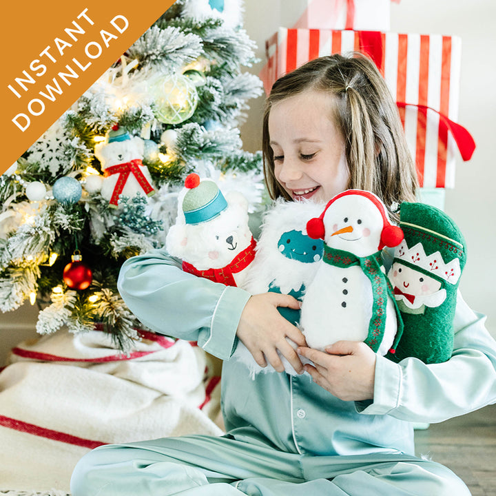 A young girl in mint green pajamas sits on the floor in front of a decorated Christmas tree, holding three plush holiday toys: a white polar bear, a white snowman with a red and green scarf, and a green elf plush. A red and white wrapped gift box is behind her, and an orange diagonal banner in the top-left corner reads 'INSTANT DOWNLOAD'.