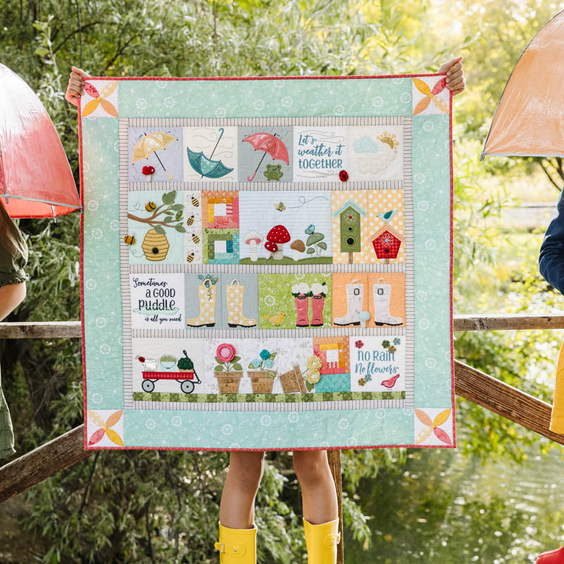 Quilt with weather-themed design held by a person outdoors