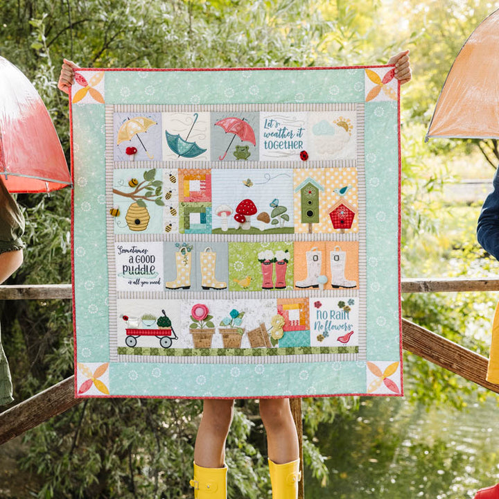 Quilt with weather-themed design held by a person outdoors