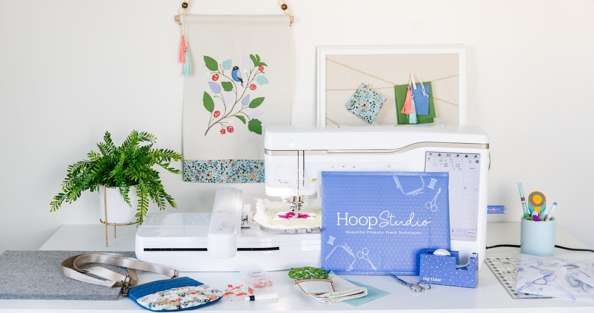 Desk with sewing machine, framed artwork, and 'Hoop Studio' branding on a white wall.
